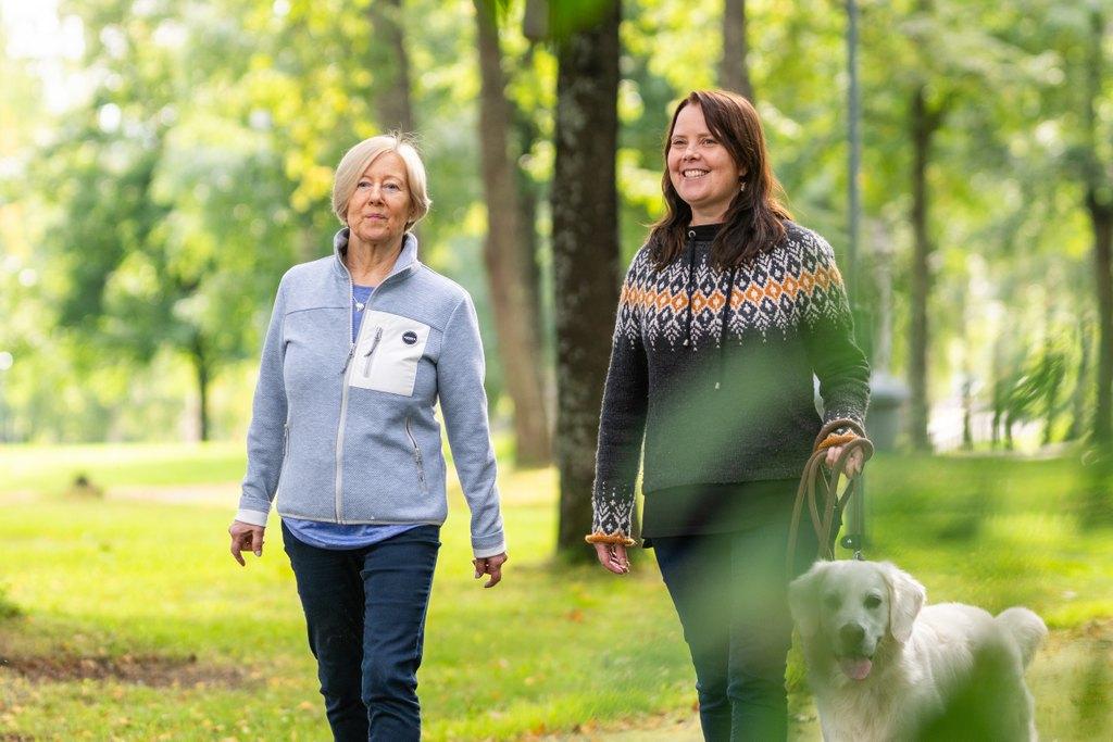 Iäkäs nainen ja keski-ikäinen nainen kävelevät puistossa ulkoiluttamassa koiraa.